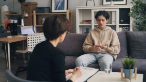 Young man sitting on a couch in deep thought, exploring how to get sober and take the first step toward addiction recovery and mental health healing